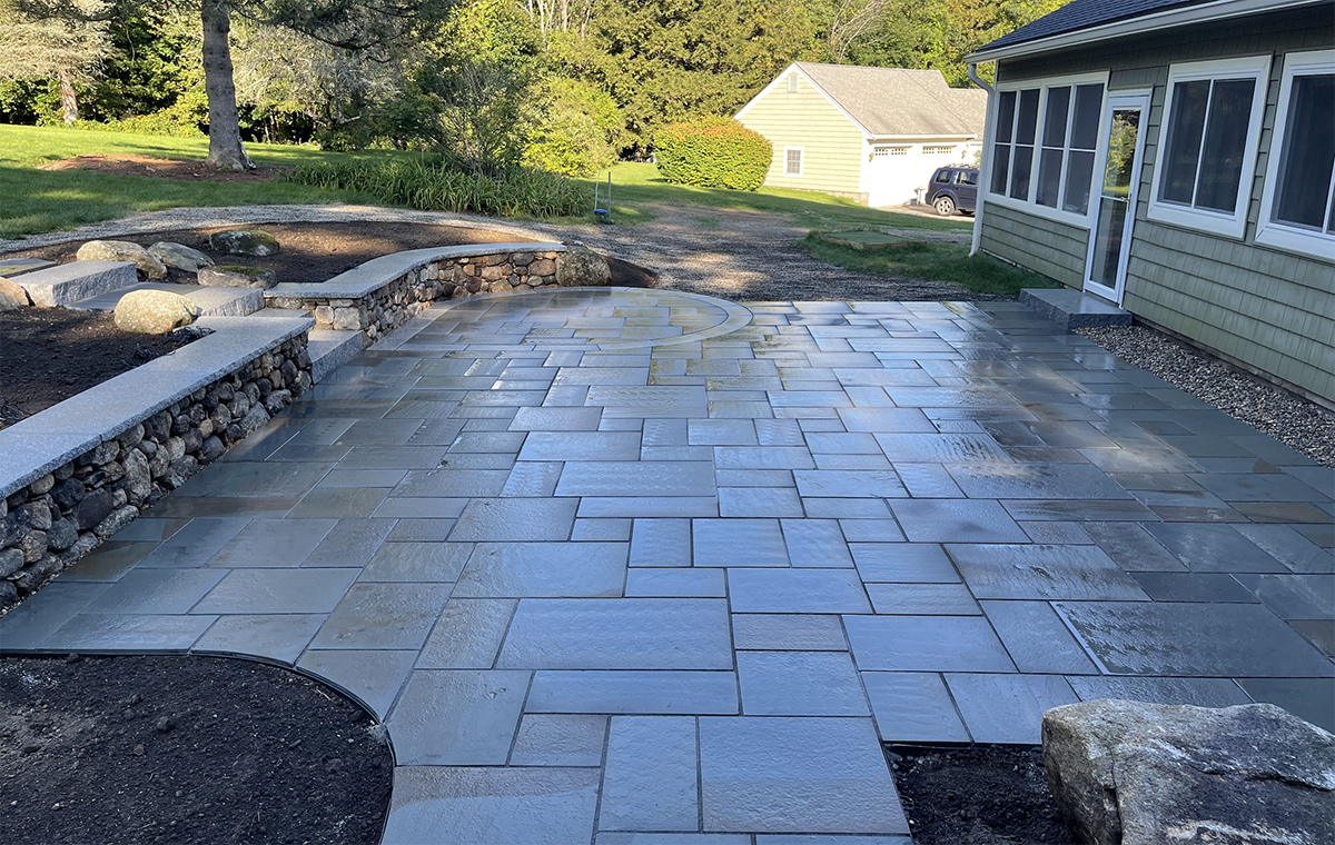 Landscape design with a bluestone patio and stone retaining wall in Bedford NH from Nest Outdoors