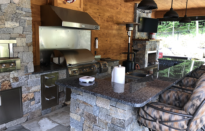 Outdoor kitchen with gas grill and bar with fireplace in Bow NH designed by Nest Outdoors